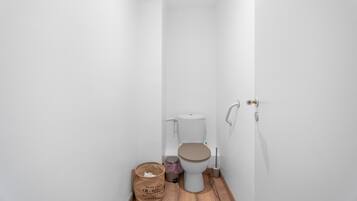 Un baño pequeño con paredes blancas, un inodoro, un cubo de basura y un paquete de pañuelos.