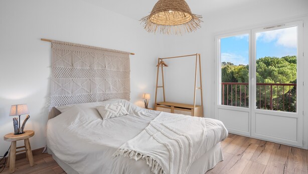 Une chambre avec un lit, une lampe suspendue, une échelle en bois, une fenêtre donnant sur un paysage verdoyant et une décoration murale.