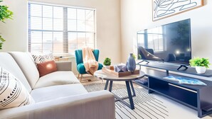 A modern living room with a sofa, armchair, coffee table, TV, and decorative items. - Boulevard Stays Spacious 1BR King Suite Pool, Gym Access & Free Parking (Irving)