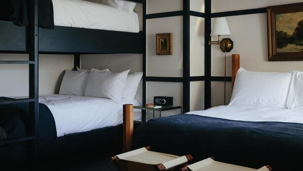 Een hotelkamer met stapelbedden, een nachtkastje met een radio, een lamp en een lijst aan de muur.