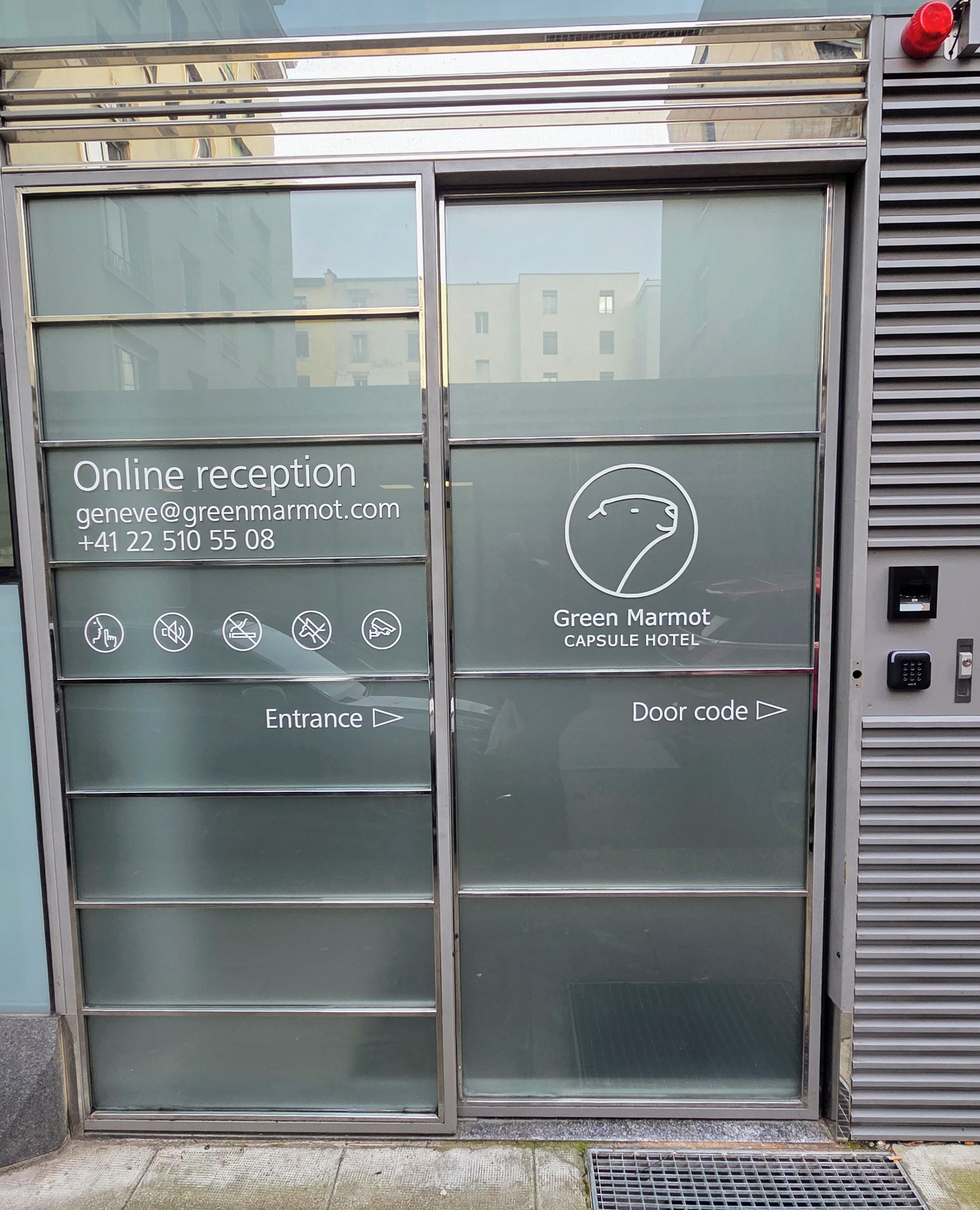 A hotel entrance with a glass door, online reception contact details, and a door code sign.