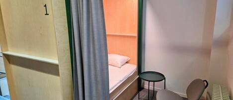 A single room with a bunk bed, a small round table, a chair, and a radiator.