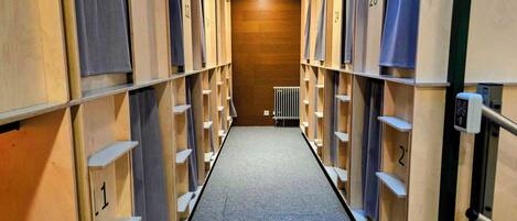 A corridor with lockers numbered 1 to 26, a radiator, and a security device on the wall.
