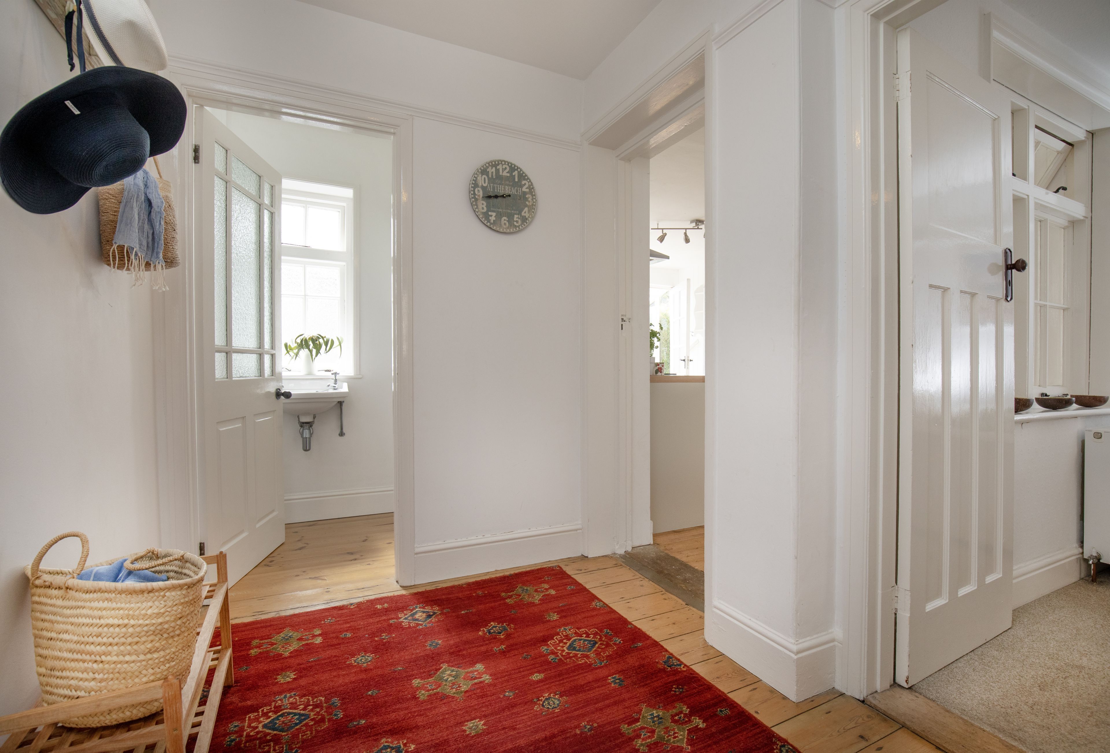 A hallway with a red patterned rug, a clock on the wall, and a door leading to a bathroom.