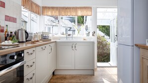 A modern kitchen with white cabinets, a wooden countertop, and a view of the outside. - Withycombe is a beautifully presented dog-friendly terraced cottage for six guests (Seaton)