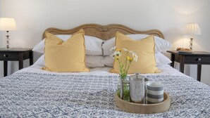 A neatly made bed with a patterned bedspread, two pillows, a bedside table with a lamp, and a tray with a vase of flowers and a mug. - Withycombe is a beautifully presented dog-friendly terraced cottage for six guests (Seaton)