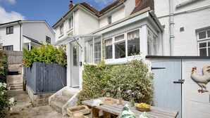 A wooden table set outdoors with a basket of fruit, a bottle, and a hat. - Withycombe is a beautifully presented dog-friendly terraced cottage for six guests (Seaton)
