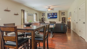 A spacious living room with a dining area, a ceiling fan, a flat-screen TV, and a sofa. - Serene Family Hideaway 4Br w Pool Table (Fortson)
