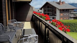 Een balkon met rieten meubilair en rode bloemen, met uitzicht op een woongebied met moderne gebouwen en een heldere lucht.