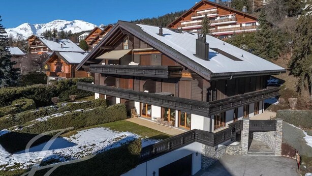 Een moderne chalet met een skilift, houten balkons en een met sneeuw bedekt dak.