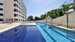 Une piscine dont le fond est recouvert de carreaux bleus, entourée d’un bâtiment blanc doté de nombreux balcons.