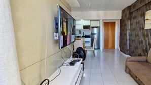 Un salon moderne avec un téléviseur à écran plat fixé au mur, un canapé et un ventilateur posé sur le sol.