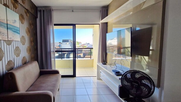 Un salon comprenant un canapé, un téléviseur à écran plat, un ventilateur et un balcon offrant une vue sur les immebles.