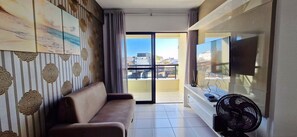 Una sala de estar con un sofá, una televisión de pantalla plana, un ventilador y un balcón con vistas a edificios.