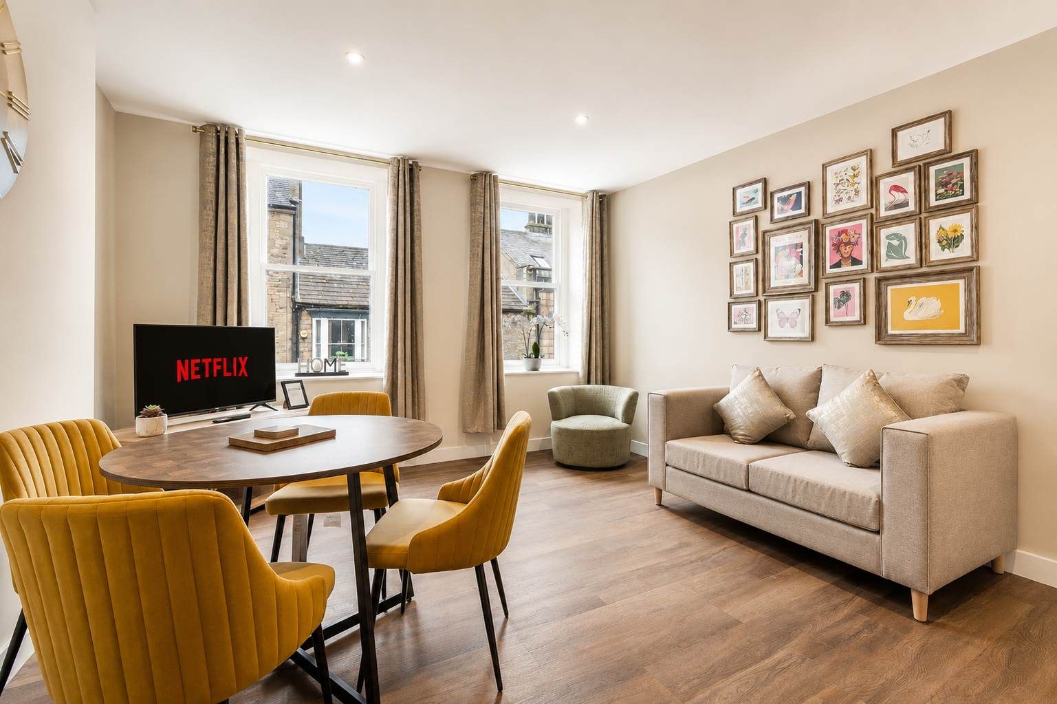 A modern living room with a round dining table, yellow chairs, a beige sofa, and a television displaying 'NETFLIX'.