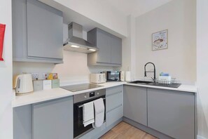 Een moderne keuken met grijze kastjes, een magnetron, een waterkoker en een spoelbak.