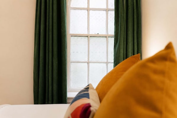 Habitació amb un llit, cortines verdes i una finestra amb vidre mat.