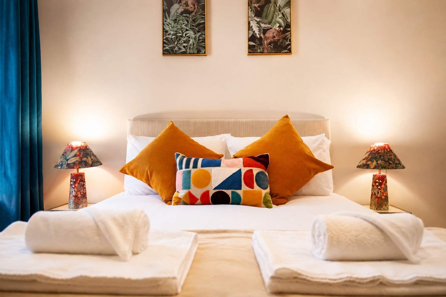 A hotel room with a bed, two pillows, a nightstand with a lamp, and two towels.