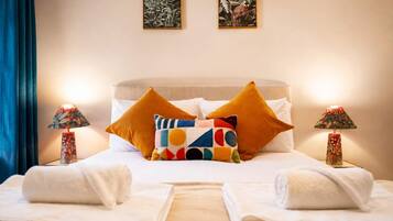A hotel room with a bed, two pillows, a nightstand with a lamp, and two towels.