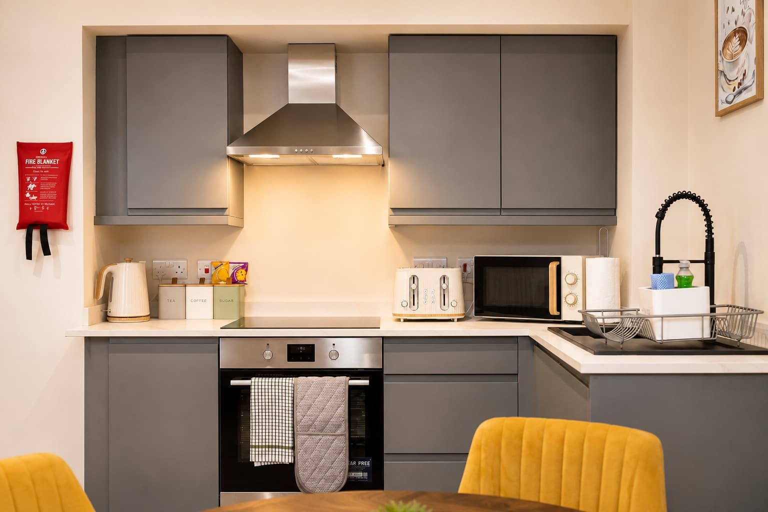 A modern kitchen with grey cabinets, a stainless steel range hood, a toaster, a microwave, and a sink with a black faucet.