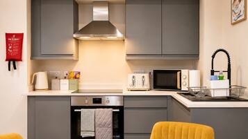 A modern kitchen with grey cabinets, a stainless steel range hood, a toaster, a microwave, and a sink with a black faucet.