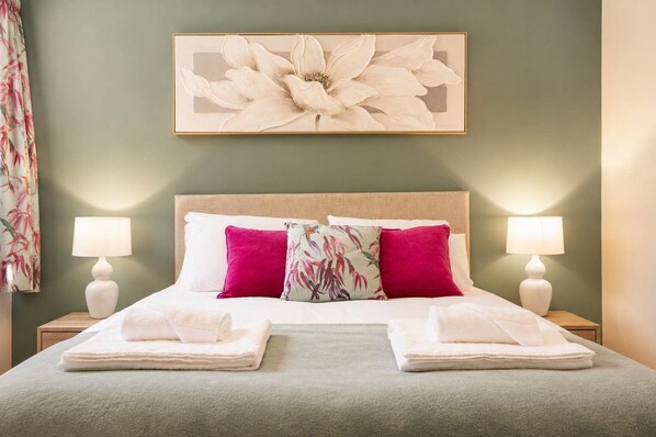 A neatly made bed with two pillows, a floral artwork above, and two bedside lamps.