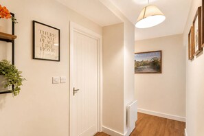 A hallway with a white door, a framed quote on the wall, a radiator, and a hanging light fixture.