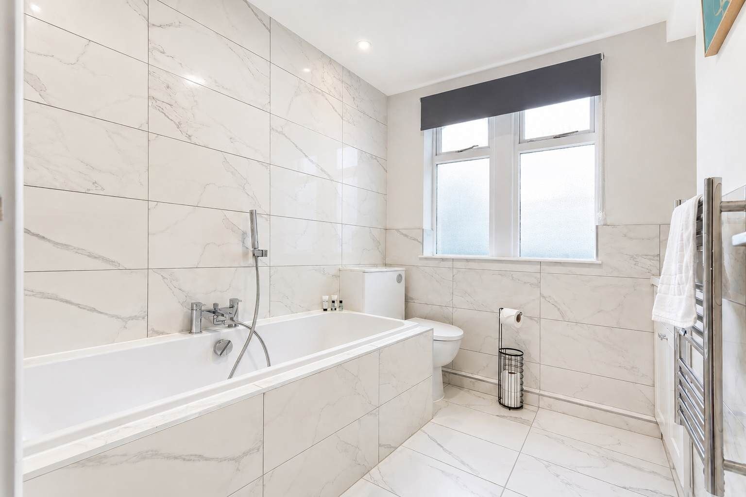 A modern bathroom with a freestanding bathtub, a toilet, and a window.