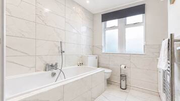 A modern bathroom with a freestanding bathtub, a toilet, and a window.