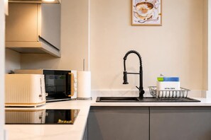 Una cuina moderna amb microones integrat, bullidor i un rentamig amb aixeta.