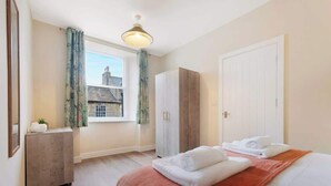 A hotel room with a bed, a wardrobe, a desk, and a window with curtains.