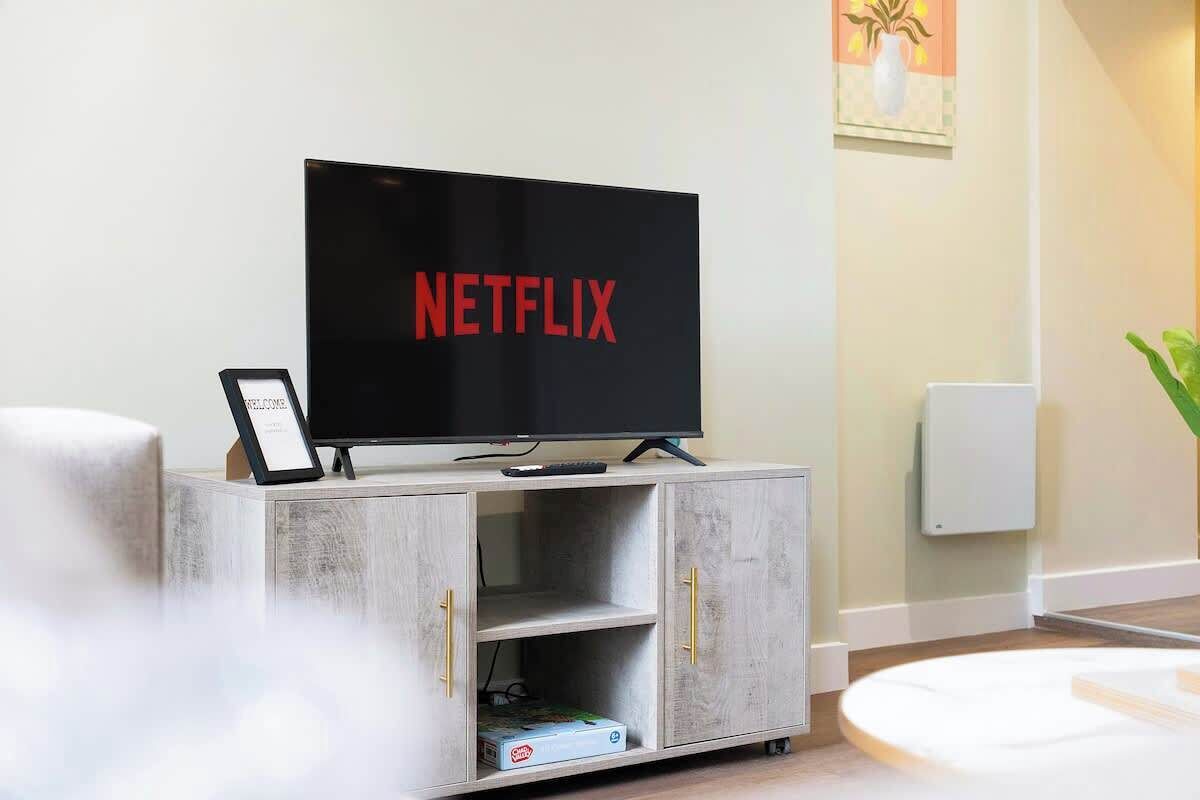 A modern living room with a flat-screen TV displaying 'NETFLIX' on the screen, a small cabinet with drawers, and a framed picture on the wall.
