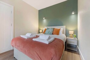 Una cama bien hecha con sábanas blancas, una pared de acento color turquesa y una mesita de noche con una lámpara.