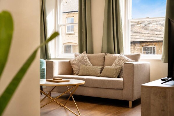 A living room with a sofa, a round coffee table, and a view of buildings through a window.