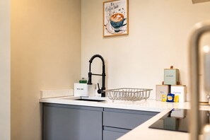A kitchen with a modern faucet, a sink, and a coffee station with labeled boxes for tea, coffee, sugar, and coffee creamer.