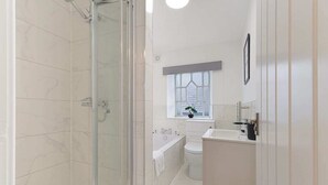 A bathroom with a glass shower enclosure, a bathtub, a toilet, and a sink.