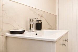Een badkamer met een witte marmeren wastafel, een chroom kraan en een zwart zeepbakje.