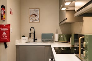 A kitchen with a sink, a fire extinguisher, a fire blanket, a coffee cup artwork, and a green appliance. - Modern 2BR | Central Barnard Castle | Sleeps 3 (County Durham)