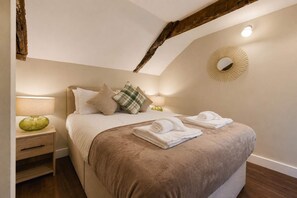 A bedroom with a bed, pillows, a bedside table, a lamp, and a wall-mounted mirror. - Modern 2BR | Central Barnard Castle | Sleeps 3 (County Durham)