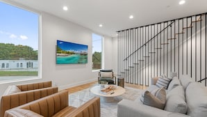 Una sala de estar moderna con un ventanal grande, una escalera y vistas a un edificio y vegetación.