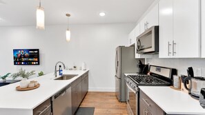 A modern kitchen with stainless steel appliances, a dishwasher, and a flat-screen TV mounted on the wall. - Trendy NoLibs Hub | Stylish 2BR Flat | Sleeps 6 (Philadelphia)