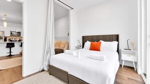 A hotel room with a bed, bedside tables, a desk, and a view into the kitchen area. - Trendy NoLibs Hub | Stylish 2BR Flat | Sleeps 6 (Philadelphia)