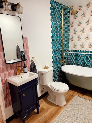 Ein Badezimmer mit einem weißen Waschbecken, einer dunkelblauen Kommode, einer weißen Toilette und einer freistehenden Badewanne.