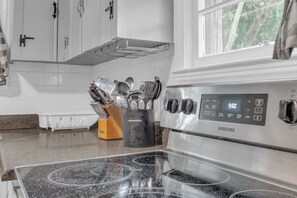 A kitchen with a stainless steel Samsung stove, white cabinets, and a window with a view of trees.