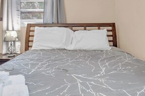 A bed with a grey and white tree branch pattern bedspread, a wooden headboard, and a nightstand with a lamp.