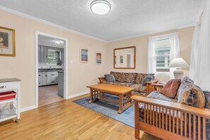 Een woonkamer met een bank, salontafel en een keuken die zichtbaar is door een open doorgang.