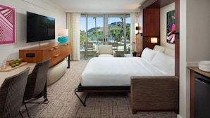 Ein Hotelzimmer mit Bett, Schreibtisch mit Fernseher, Stuhl und Blick auf Strand und Berge.