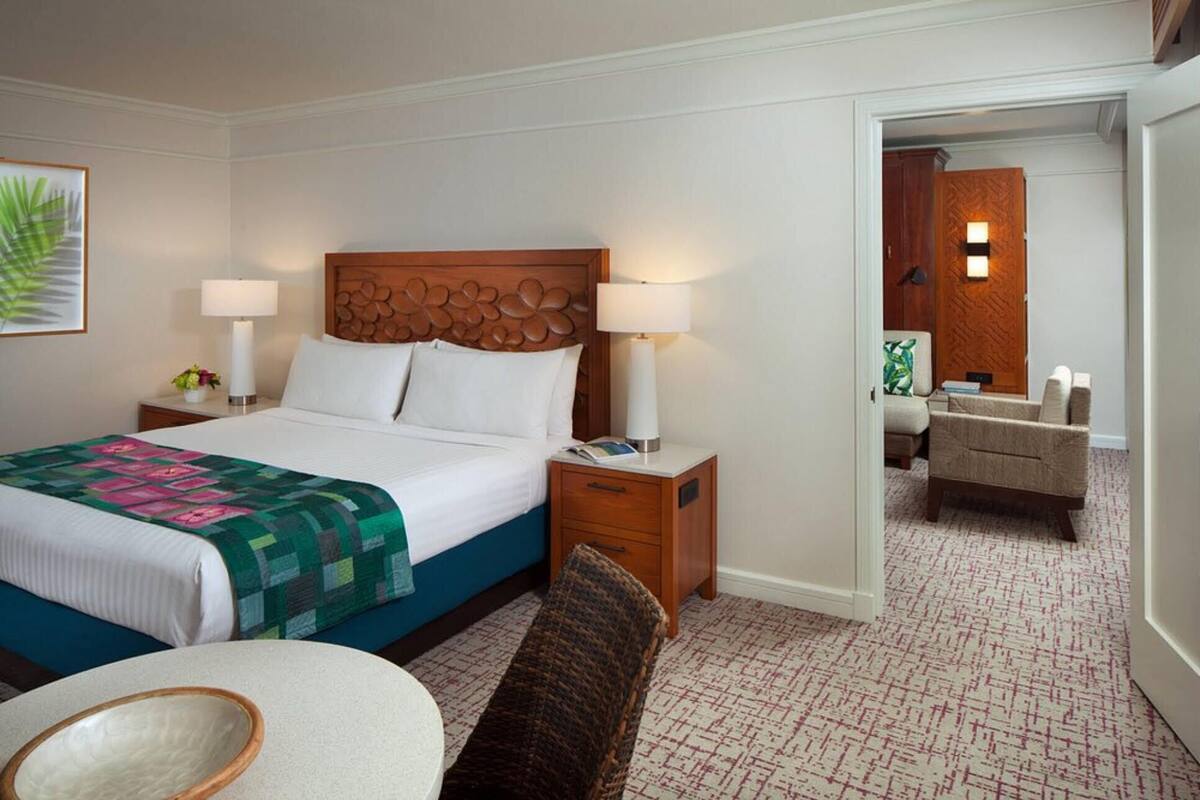 Una habitación de hotel con una cama grande, dos mesitas de noche con lámparas, una silla, una pequeña mesa y un espejo.