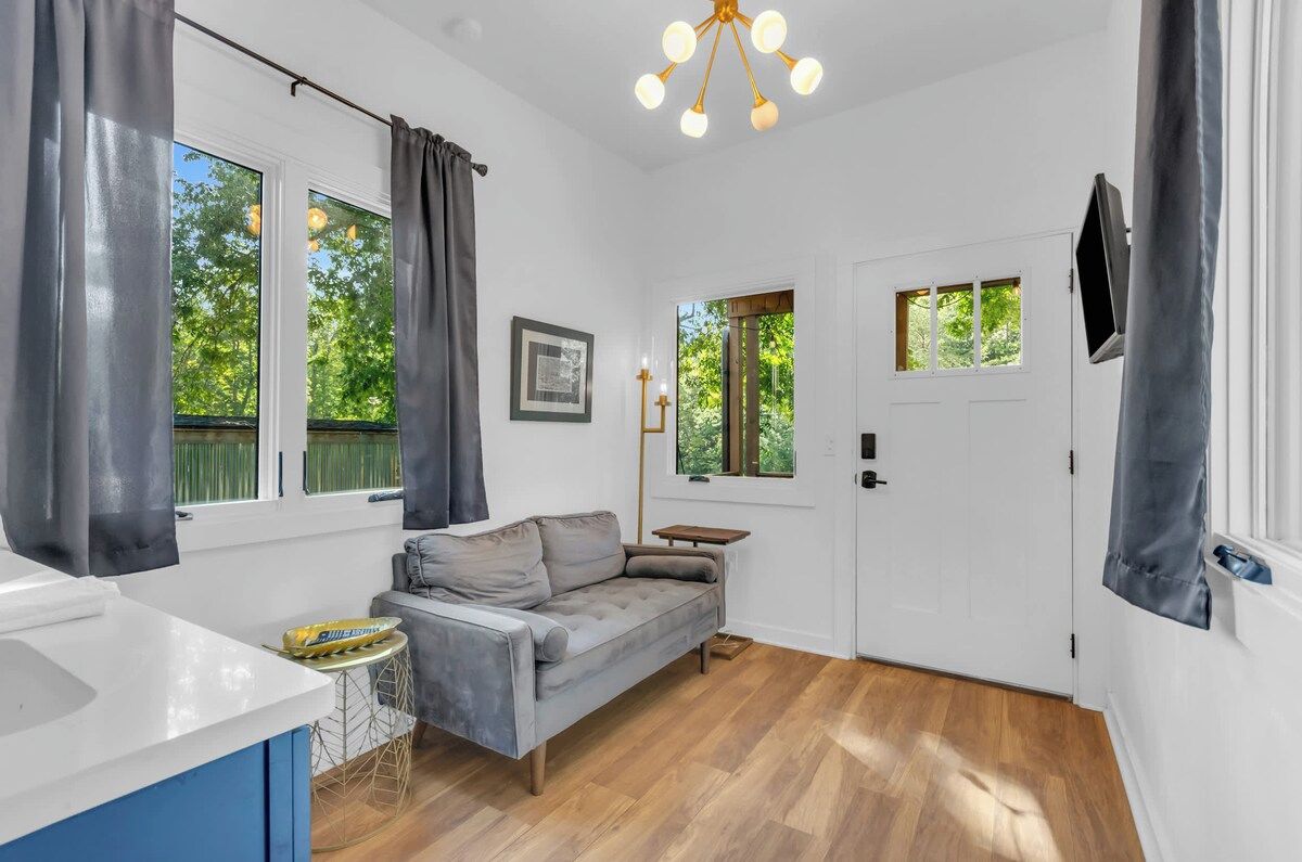 A room with a grey sofa, a white door, and a window with curtains.