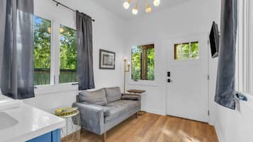 A room with a grey sofa, a white door, and a window with curtains.